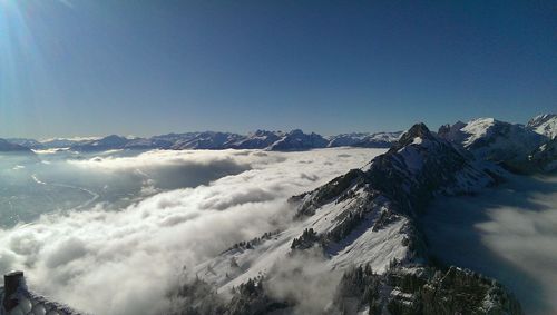 Scenic view of cloudscape covering snow covered mountains against clear blue sky