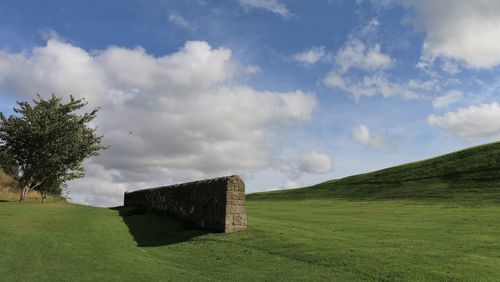 Built structure on grassy landscape against clouds