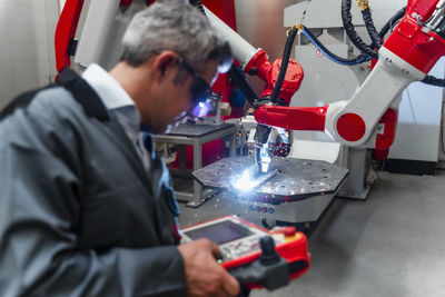 Mature worker using control in front of robotics in factory