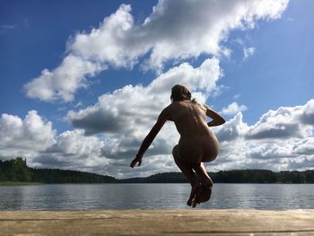 Naked woman jumping at lake against sky