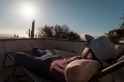 Man lying on chair against sky