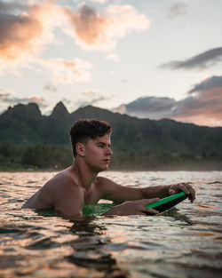 Portrait of shirtless young man in mountains against sky