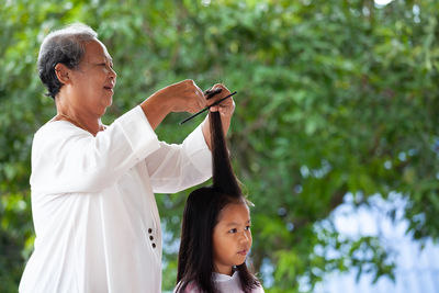 Grandmother combing granddaughters hairs outdoors