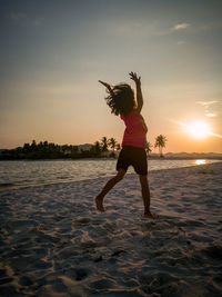 Full length of woman jumping on beach against sky during sunset