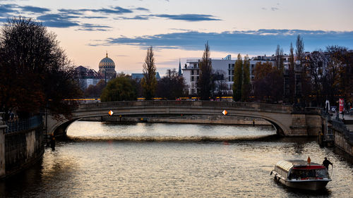 Bridge over river in city against sky during sunset