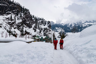 Rear view of people walking on snow covered mountain against sky