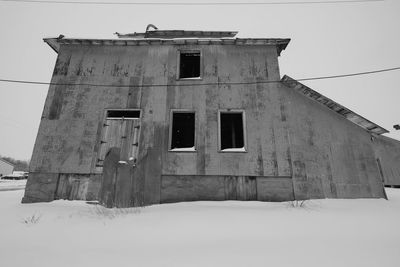 Low angle view of abandoned building on snow covered field against sky