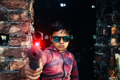 Portrait of boy holding camera against wall