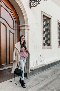 Full length portrait of smiling woman standing at entrance of building