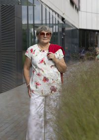 Real modern senior woman in sunglasses walks near shopping mall. portrait of happy elderly female