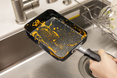 The dirty frying pan is being washed in the kitchen sink