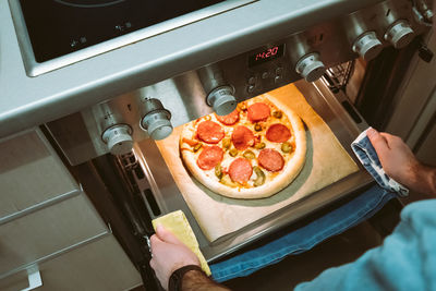 Elevated view of men's hands pulling a finished homemade pizza out of the oven