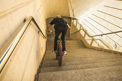 Rear view of young man riding bicycle on steps