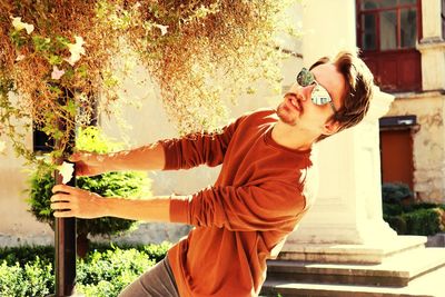 Young man wearing sunglasses hanging by plant