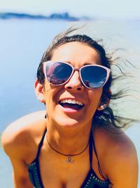 Portrait of cheerful woman wearing sunglasses at beach during sunny day