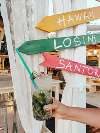 Woman's hand holding mojito cocktail in front of colorful signpost in beach bar.