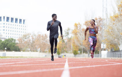 Happy male and female athlete running on track against clear sky