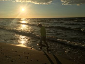 Rear view of man standing at beach during sunset