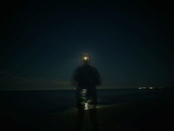 Rear view of man looking at sea against sky at night