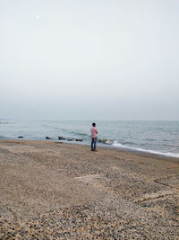 Rear view of man standing on concrete shore looking at horizon