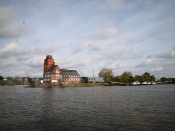 View of buildings by river against cloudy sky