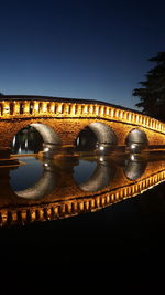 Illuminated bridge over river against sky at night