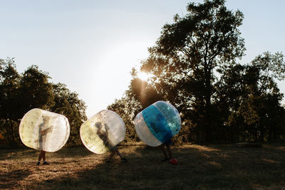 Friends playing in bubble football at park against clear sky 