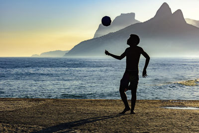 Silhouette man standing at beach against sky during sunset