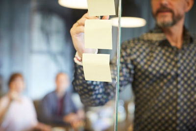 Midsection of businessman writing on adhesive note stuck to glass in creative office