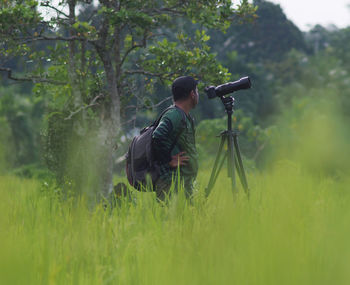 Man with camera on tripod standing at field