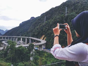 Man photographing with mobile phone against mountains