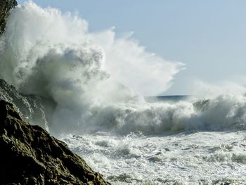 Waves splashing on rocks against sky
