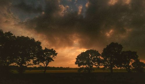 Silhouette trees on field against storm clouds