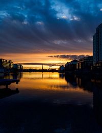 Scenic view of river by buildings against sky at sunset