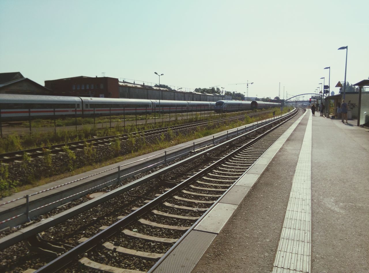 railroad track, transportation, clear sky, the way forward, vanishing point, rail transportation, diminishing perspective, building exterior, built structure, copy space, sky, architecture, road, public transportation, outdoors, railway track, day, road marking, empty, no people