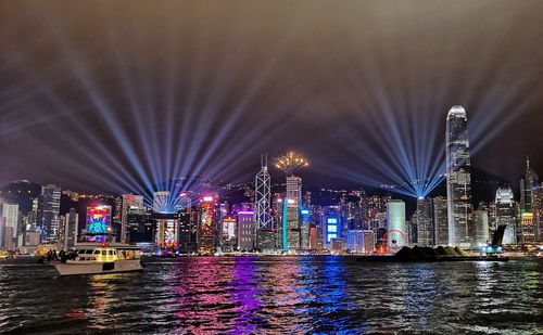 Illuminated buildings by river against sky at night