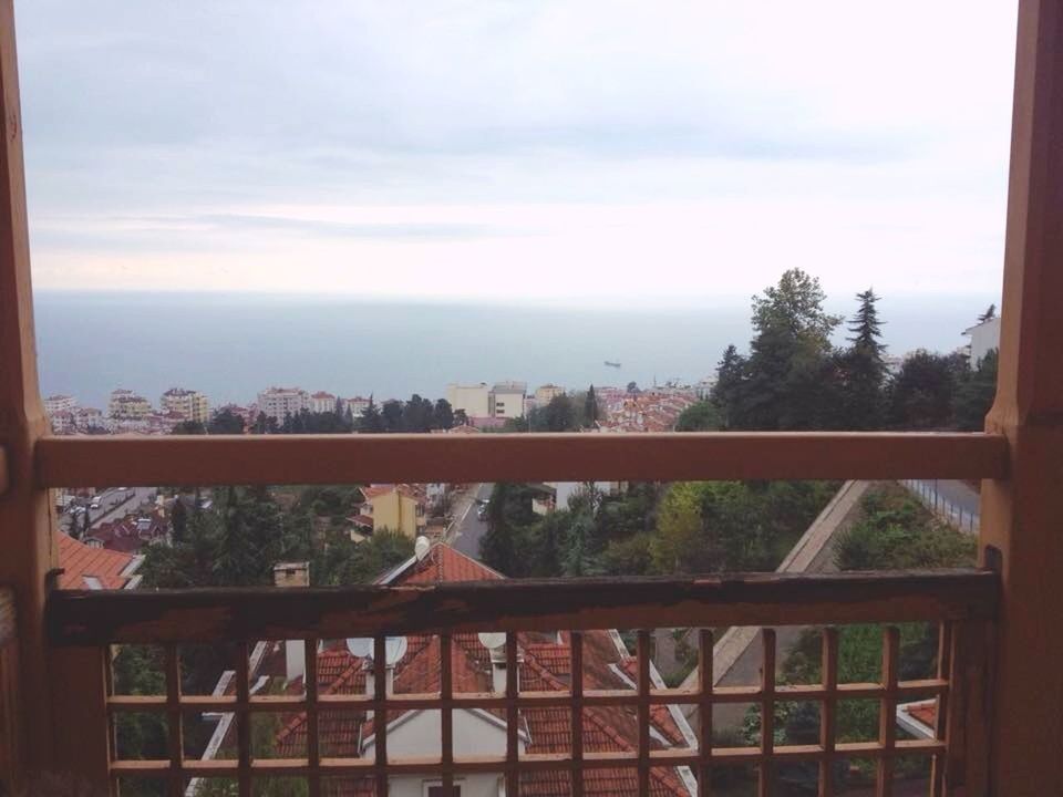 sky, window, tree, built structure, architecture, indoors, cloud - sky, sea, glass - material, railing, transparent, cloud, building exterior, day, balcony, nature, horizon over water, no people, city, water