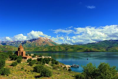 Castle by lake and mountains against blue sky
