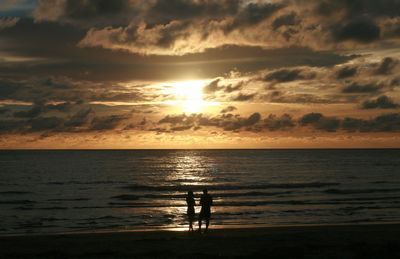 Silhouette people standing on beach against sky during sunset