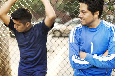 Men looking away while leaning on fence at soccer field