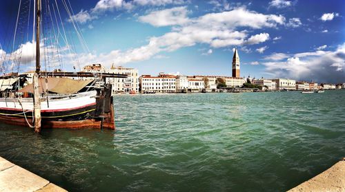 Sailboats moored in sea by city against sky