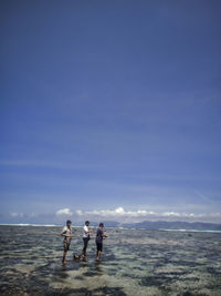 People angling while standing in sea against sky