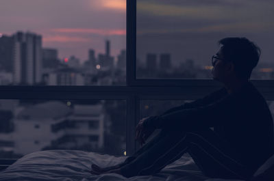 The man sitting on bed with city view from bedroom. stay home, depression and loneliness concept.