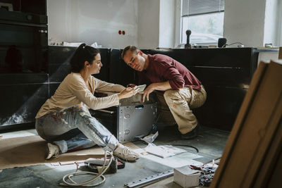 Couple discussing over mobile phone while renovating kitchen at home