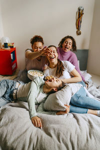 Playful female friends watching tv while enjoying snacks at home