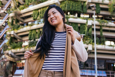 Portrait of smiling young woman standing against city