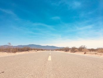 Road leading towards desert against blue sky