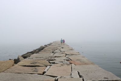 Rear view of man walking by sea against sky