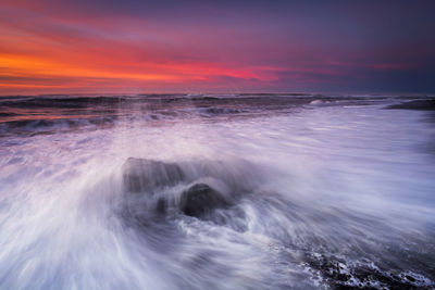 Long exposure image of sea waves against sky during sunset