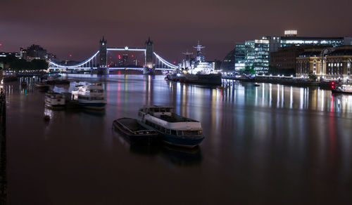 Illuminated bridge over river in city against sky at night